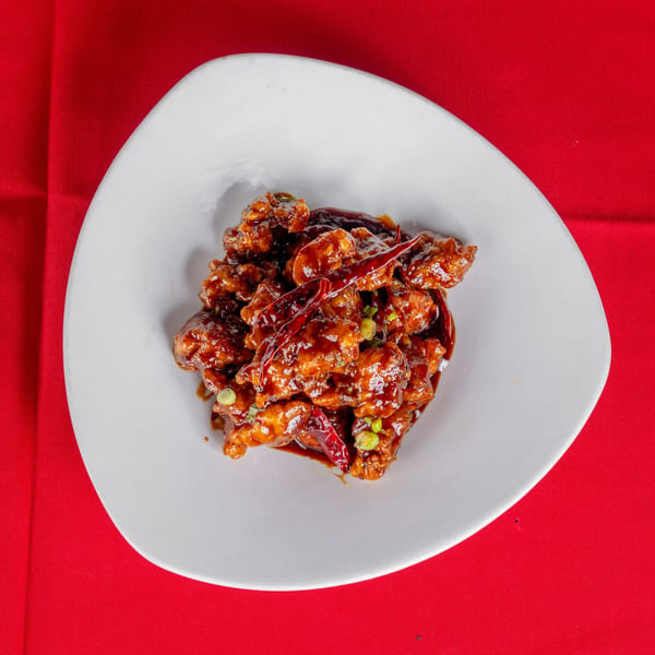 Spicy General Tso's chicken with red chili peppers and scallions on a white plate.