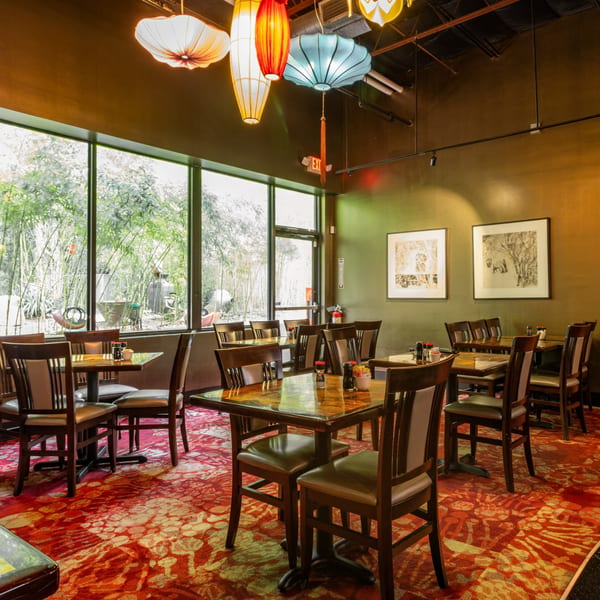 Restaurant dining room with tables, chairs, red patterned carpet, and large windows overlooking bamboo.