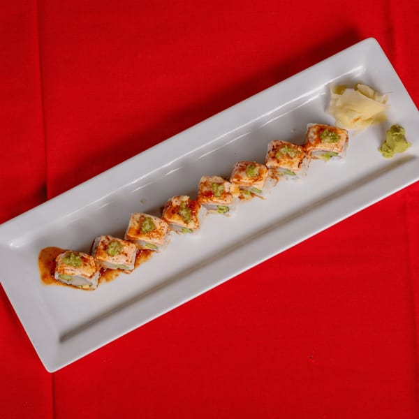 Sushi roll pieces with salmon, green sauce, and spicy sauce on a white plate with wasabi and ginger.