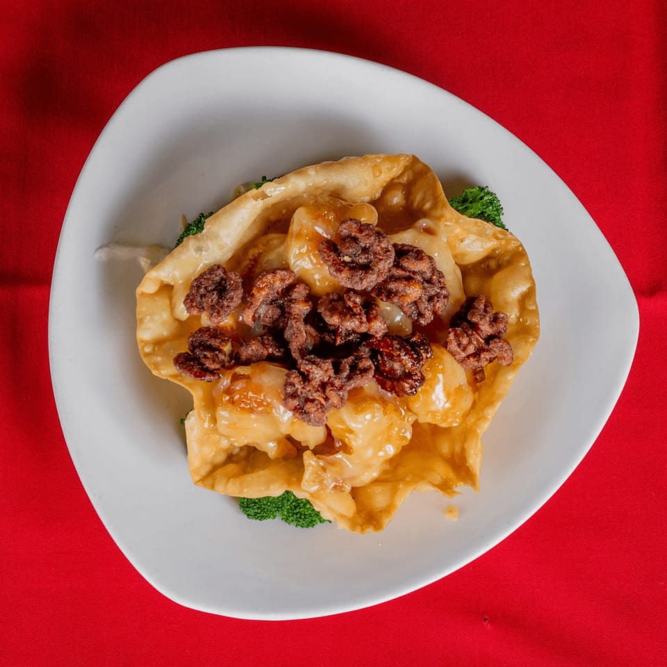 Crispy wonton bowl filled with shrimp, glazed walnuts, and a creamy sauce on a red tablecloth.