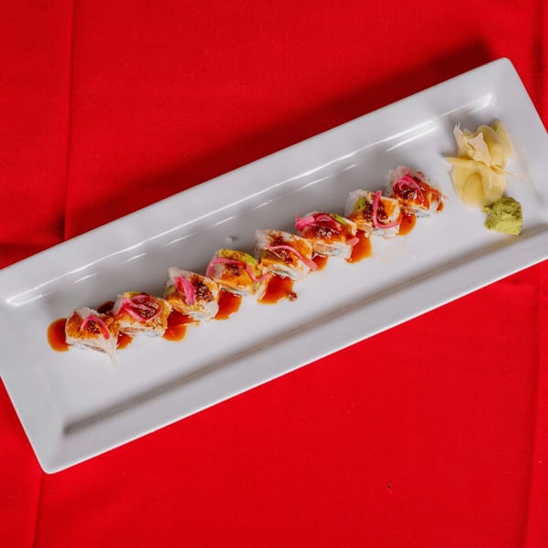 Sushi roll slices with sauce, pink pickled onions, ginger, and wasabi on a white plate.
