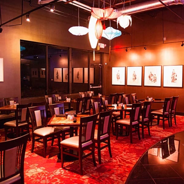 A restaurant dining room with red patterned carpet, dark tables, chairs, and hanging lanterns.