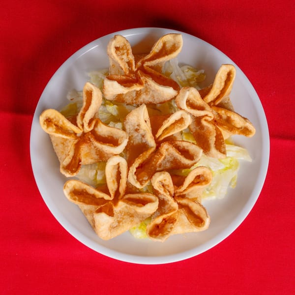 A white plate with several golden-brown crab rangoon appetizers on a bed of shredded lettuce, against a red tablecloth.