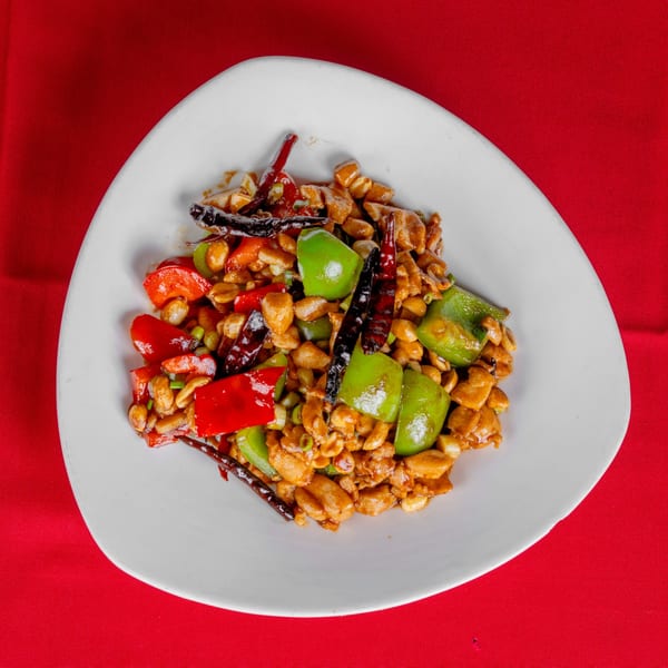 Kung Pao Chicken with peanuts, red and green bell peppers, and dried chilies on a white plate.