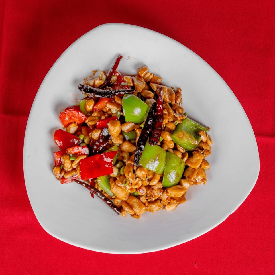 Kung Pao chicken with peanuts, red and green bell peppers, and dried chilies on a white plate.