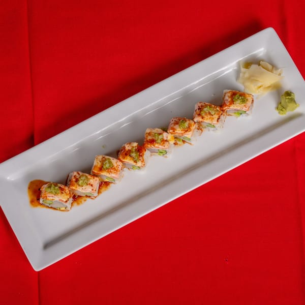 Sushi rolls with seared salmon, green sauce, and spicy drizzle on a white plate with ginger and wasabi.