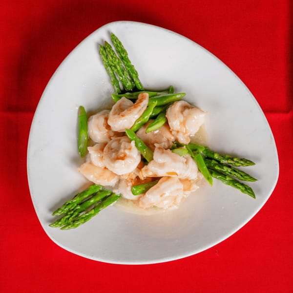 Shrimp and asparagus stir-fry in a light sauce, served on a white plate over a red tablecloth.