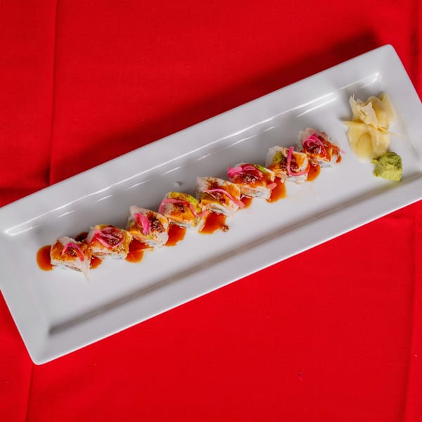 Sushi roll with avocado, pink pickled onions, and sauce, served with ginger and wasabi.
