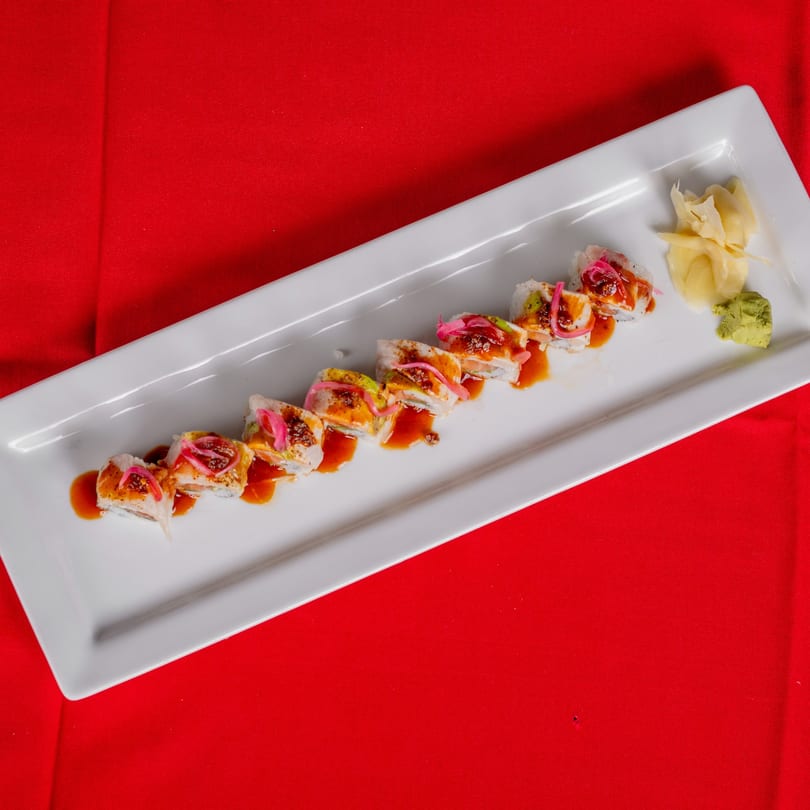 Sushi roll with avocado, pink pickled onions, and sauce, served with ginger and wasabi.